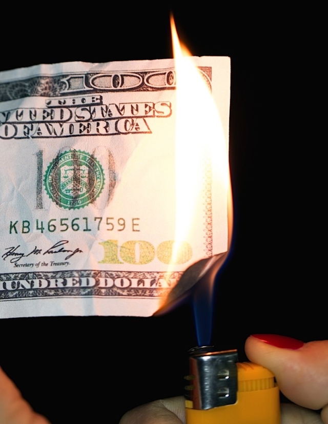 Hundred dollars burning on a black background . Photo courtesy of BigStock/schankz