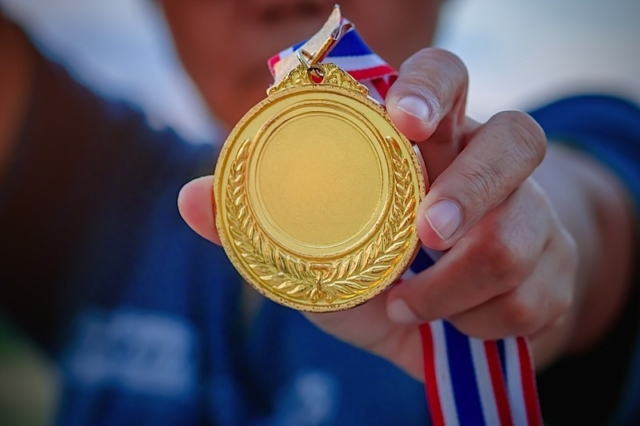 Number 1 winner hand raised and holding old gold medals award winner concept Photo courtesy of BigStock/smolaw