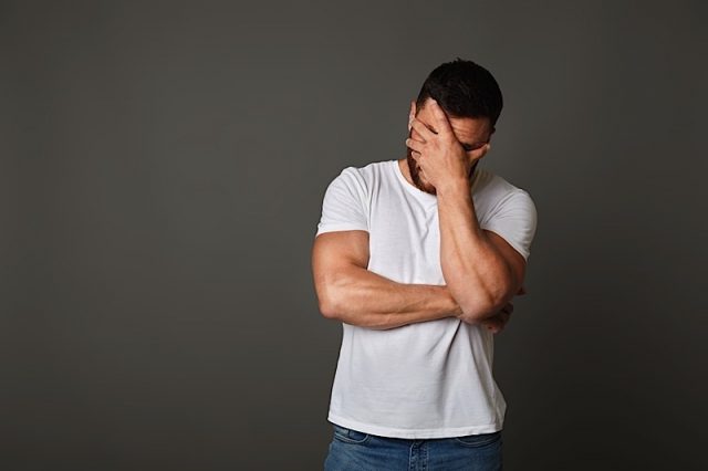 Young Man With Facepalm Gesture. Disappointed Stressed Guy In White T-shirt Covering Face With Hand Young man with facepalm gesture. Disappointed stressed guy in white t-shirt covering face with hand on studio background, copy space