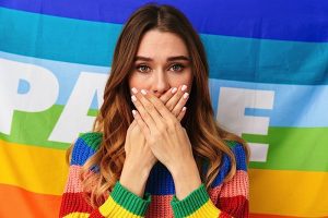Upset, worried young woman with a Pride flag behind her.