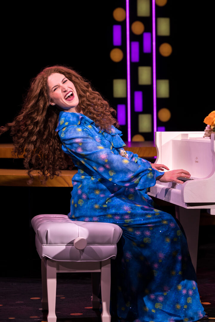 Monet Sabel as Carole King on stage playing piano.