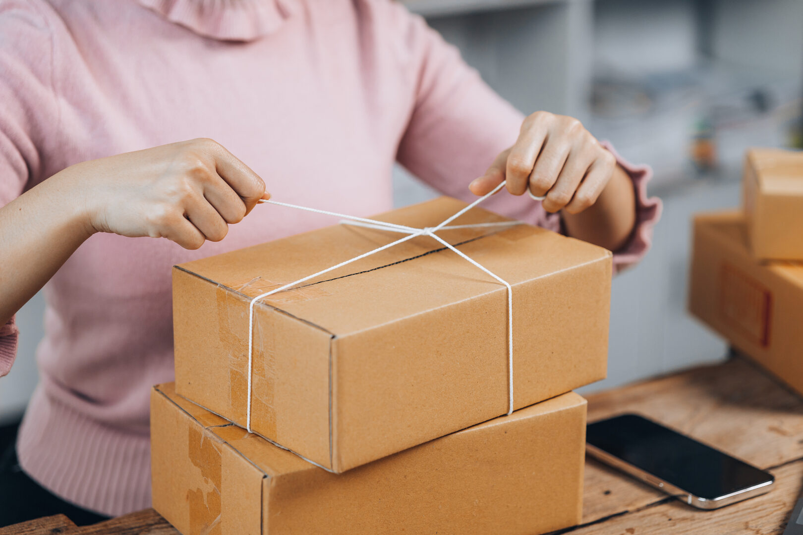 Woman tying up a packing box, getting it ready to be shipped.