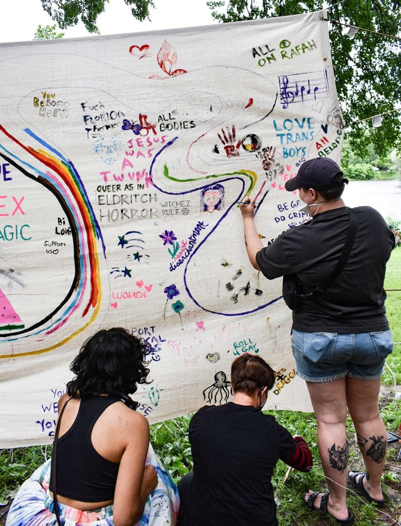 Woman drawing on a hanging sheet with art and messages of care.