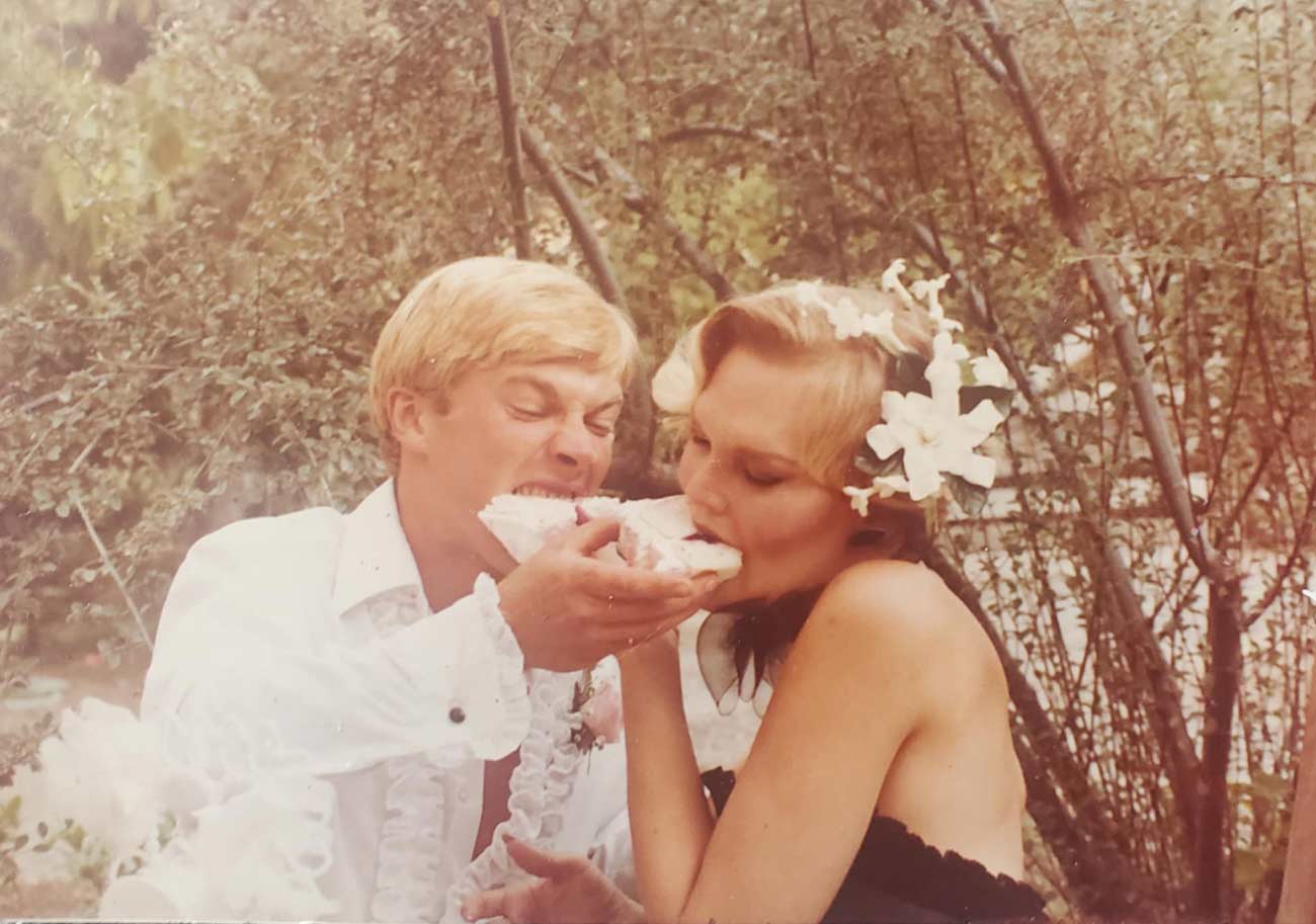 A young Julie and man shoving cake in each others mouths.