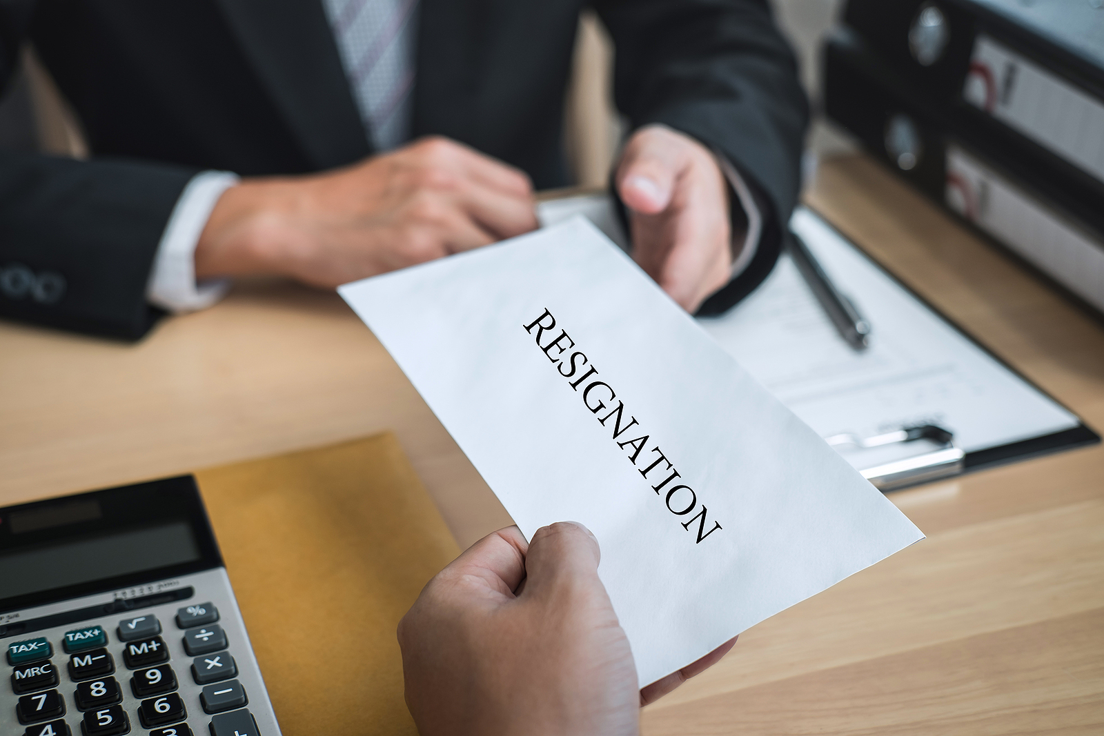 Person handing in an envelope to their boss announcing their resignation.