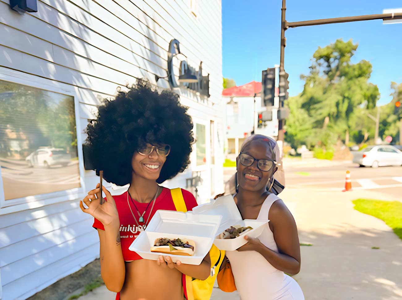 Two happy women holding hot dogs at a small festival.