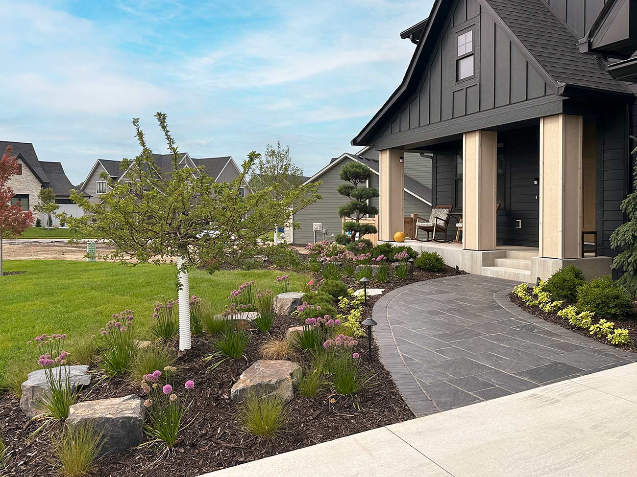 Sidewalk leading to house landscaped with flowers, rocks, and shrubs.