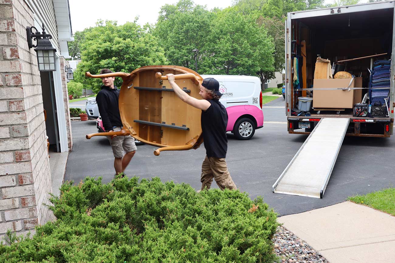 Two men moving a dining room table from a moving truck.