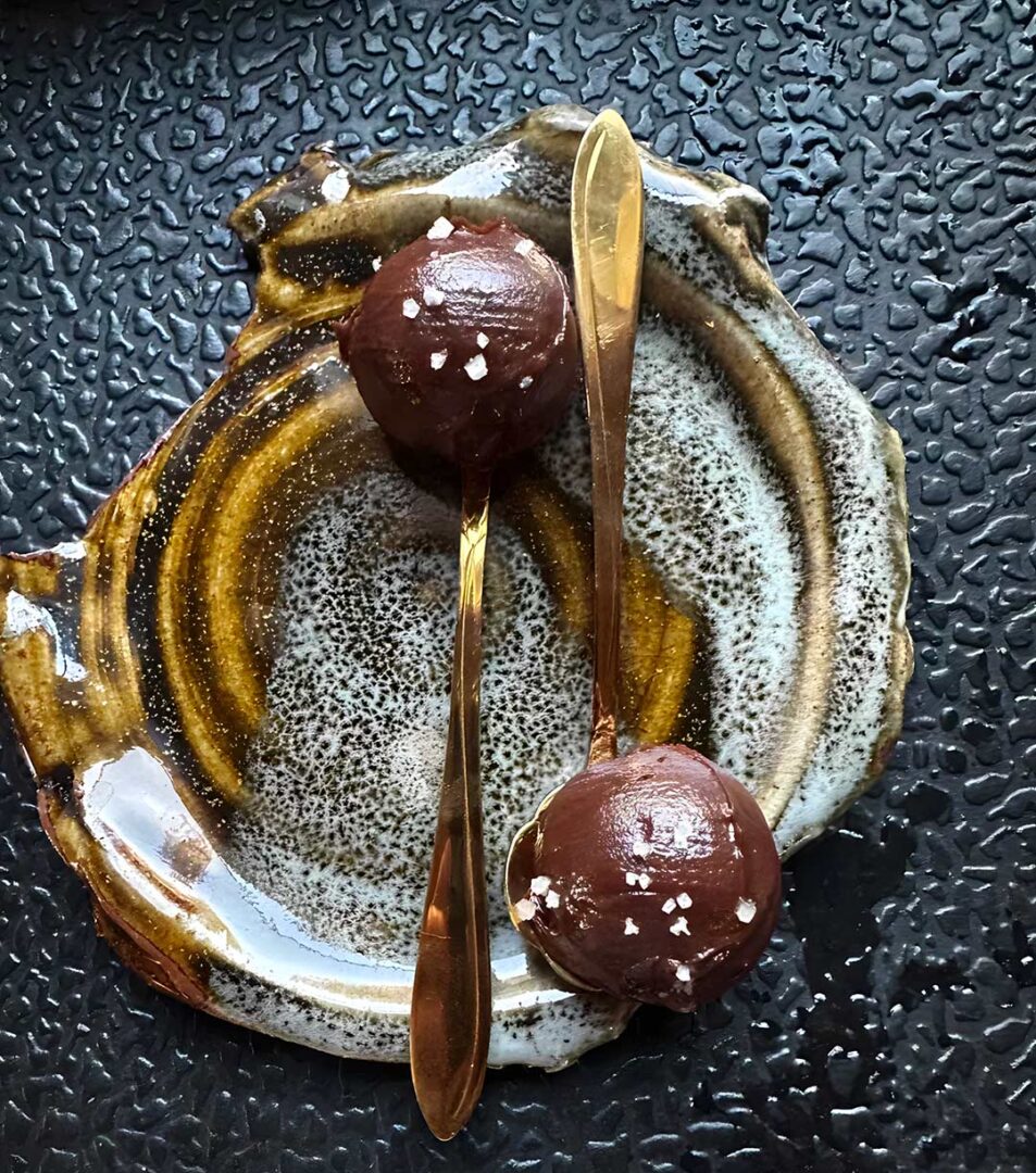 Chocolate truffles on the end of golden spoons with a gold glitter smear underneath them.