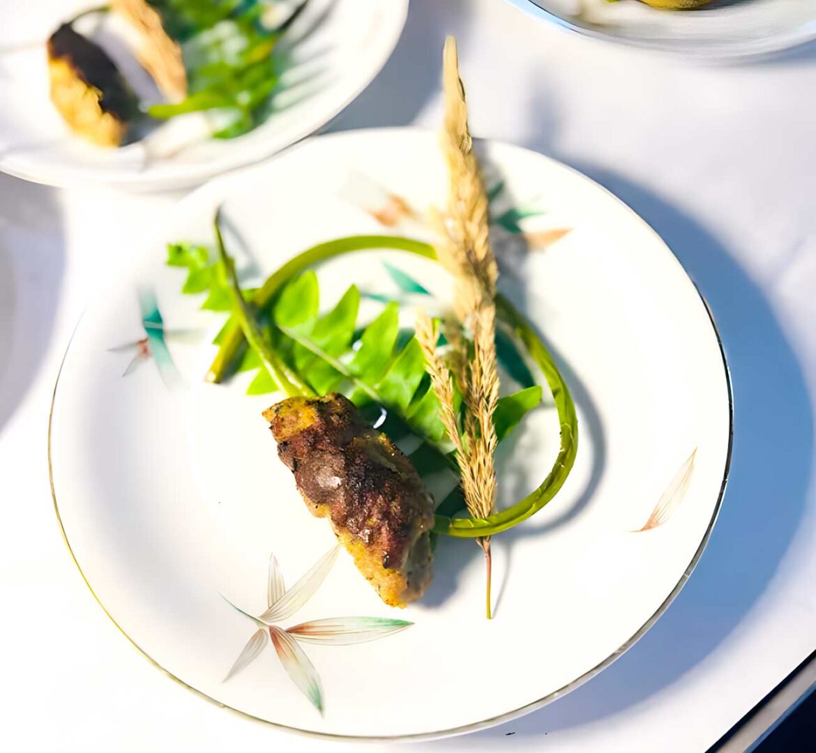 Elegant plate with fern prawn and wheat tip alongside a small cut of meat.