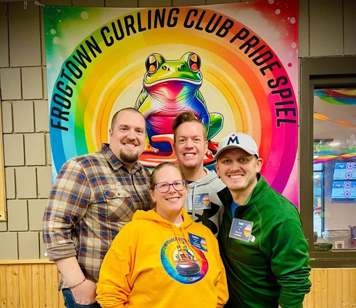 Four coordinators of the Frogtown Curling Club Pride Spiel pose in front of their teams banner.