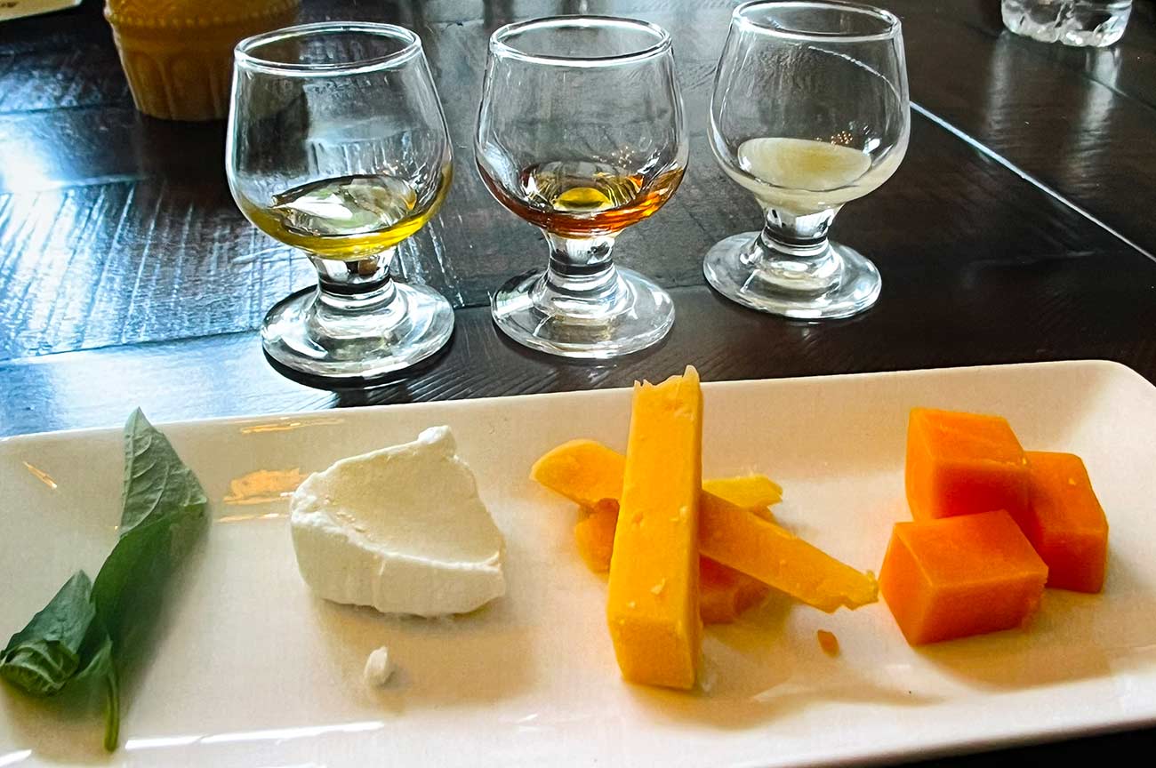 Small glasses with honey in front of a small plate of cheeses at a honey tasting.
