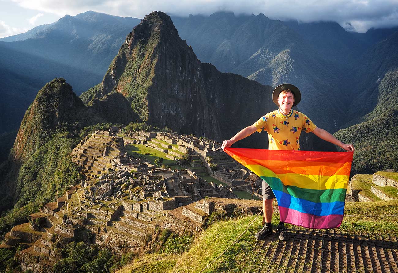 Mikah holding a rainbow flag with the city of Machu Picchu in the background.