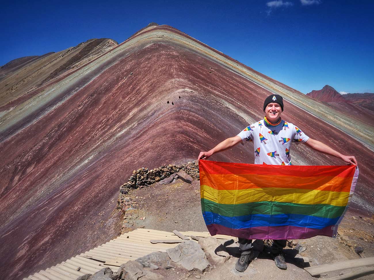 Mikah holding a rainbow flag with the Rainbow Mountains behind him.