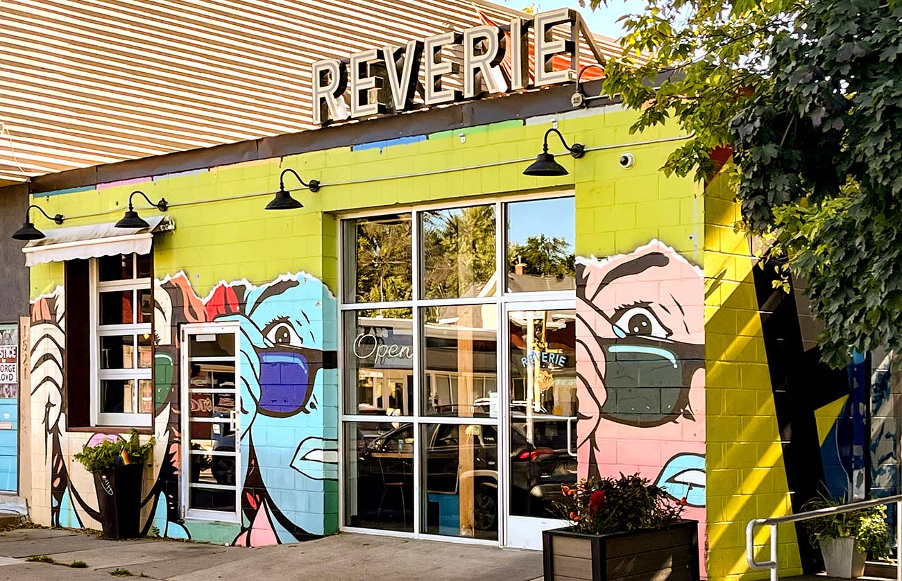 Exterior view of the restaurant Reverie with three of the same face mural of a worried womans face pulling down her sunglasses.