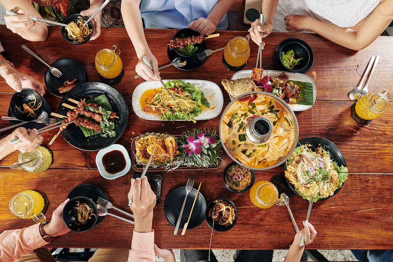 Big Asian family eating various tasty dishes and snacks with chopsticks at restaurant table.