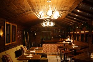 Nighttime shot of a dining room in a Nordic Lodge featuring antler chandeliers.