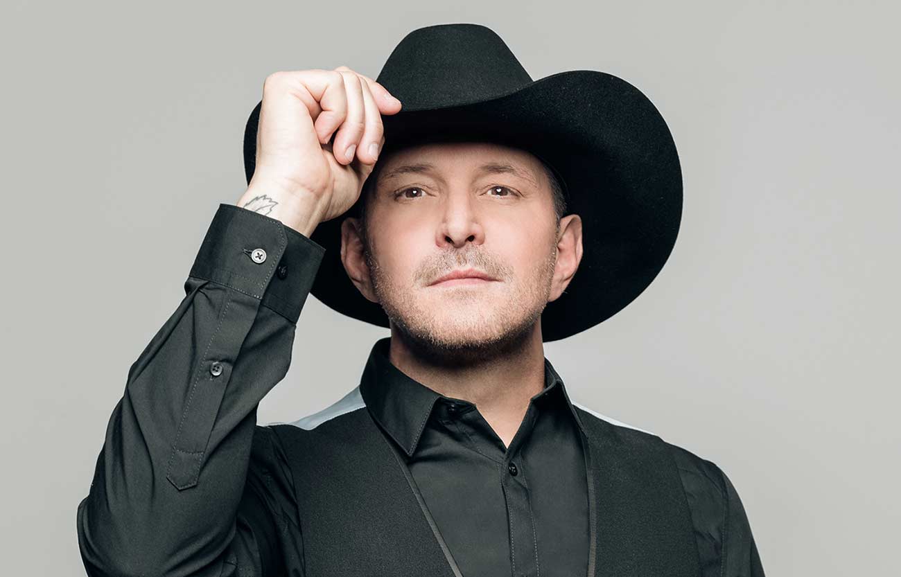 Gay country artist Ty Herndon holding the rim of his hat for a promo shot.