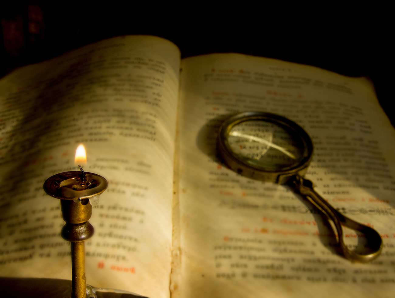 Candle fades over the old prayer book with a magnifying glass.