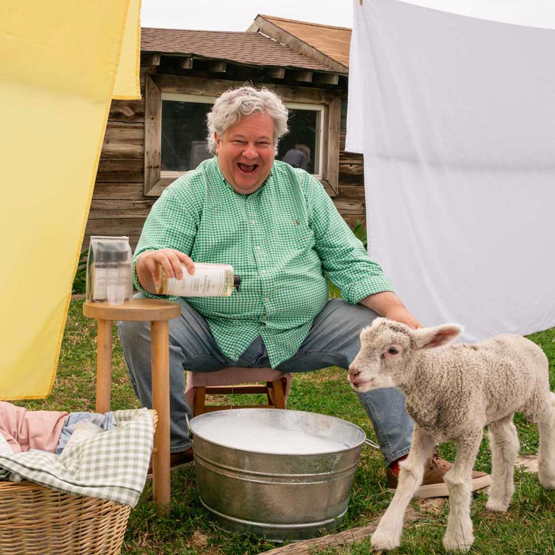 Patric Richardson during soap into a metal tub with a lamb standing next to him.