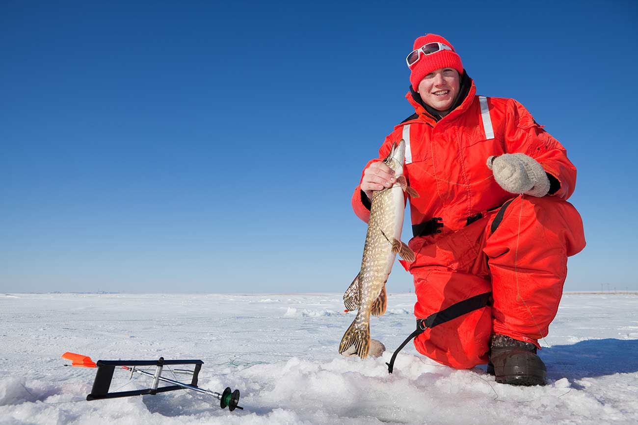 Ice fisherman holding a northern pike caught on a tip up.
