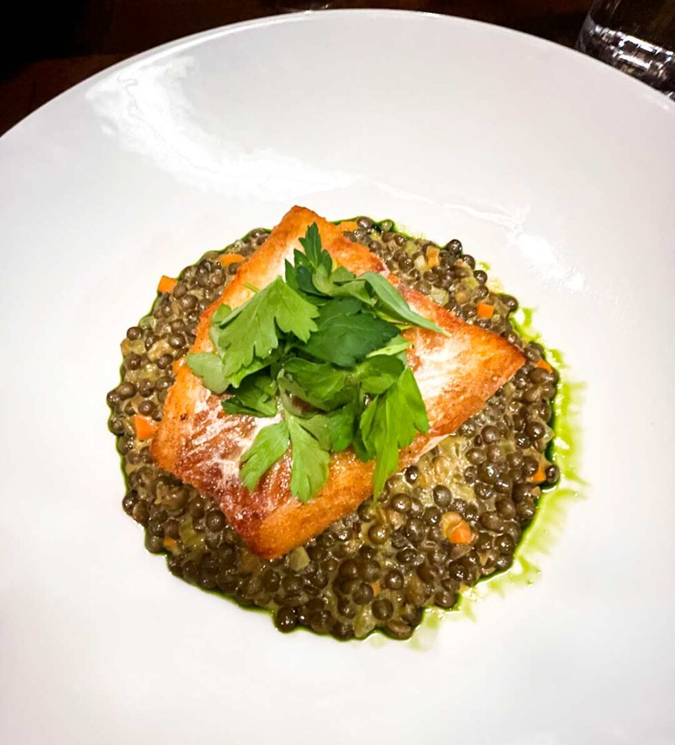 Piece of cod on a bed of lentils and garnished with parsley.