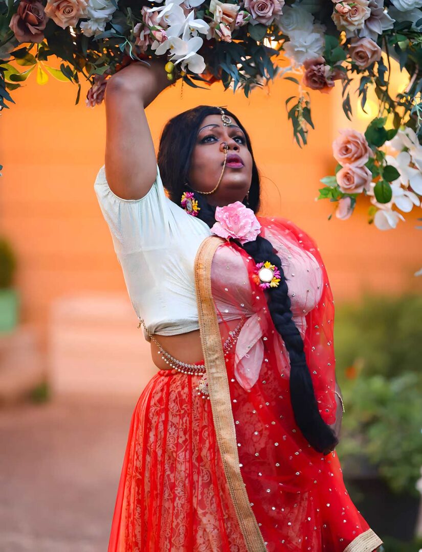 South Indian Drag Artist Silukku under an arch of flowers.