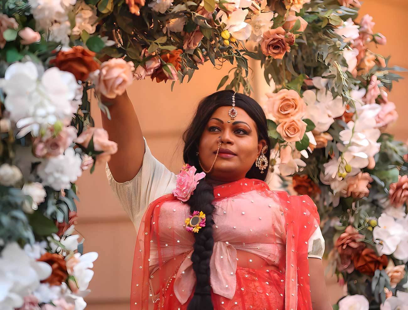South Indian Drag Artist Silukku picking a flower from a flower archway.
