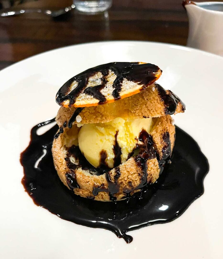 Profiterole puff with ice cream in the middle and drizzled with chocolate.