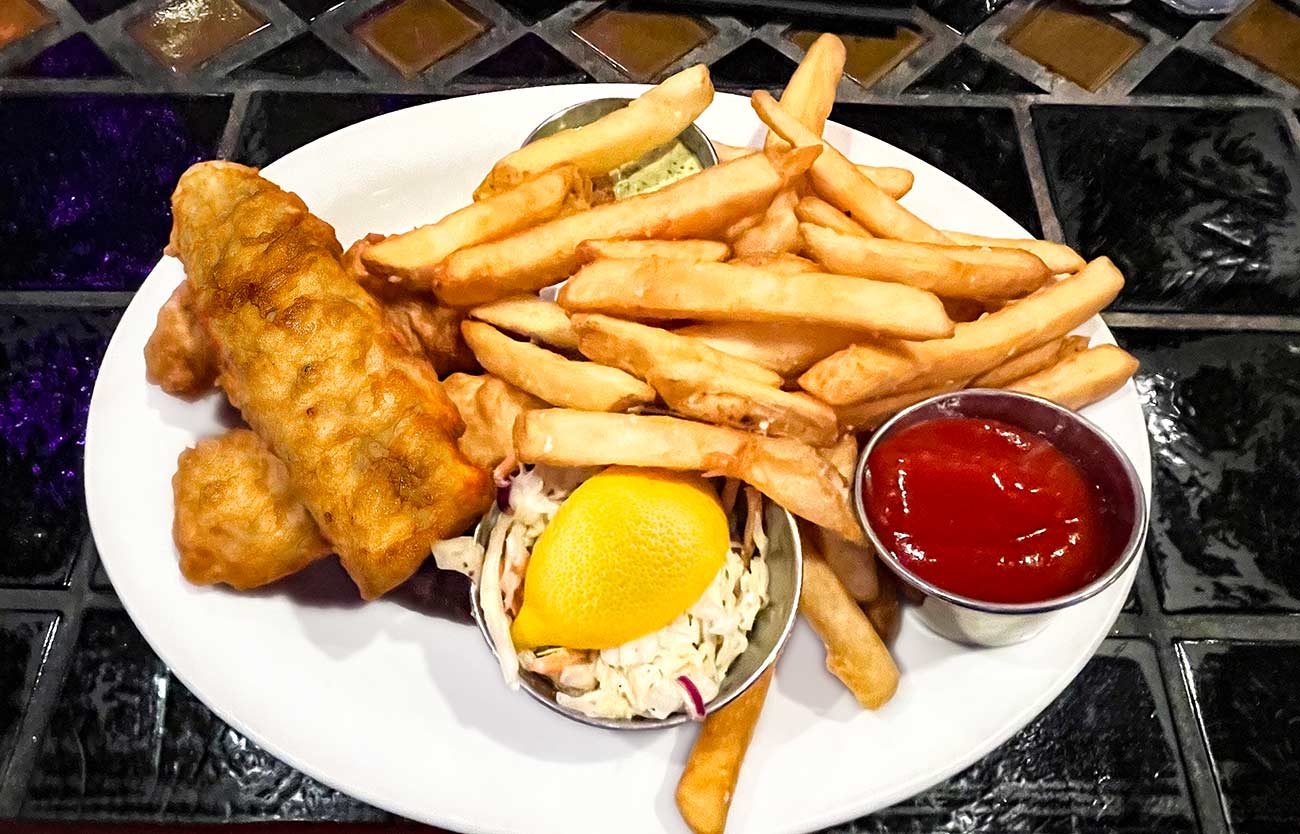 Plate with beer battered cod with lemon wedge, coleslaw and french fries with ketchup.