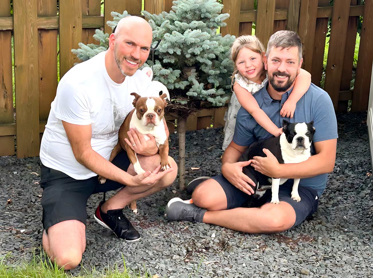 Male queer couple sitting in their garden with their dog and daughter.