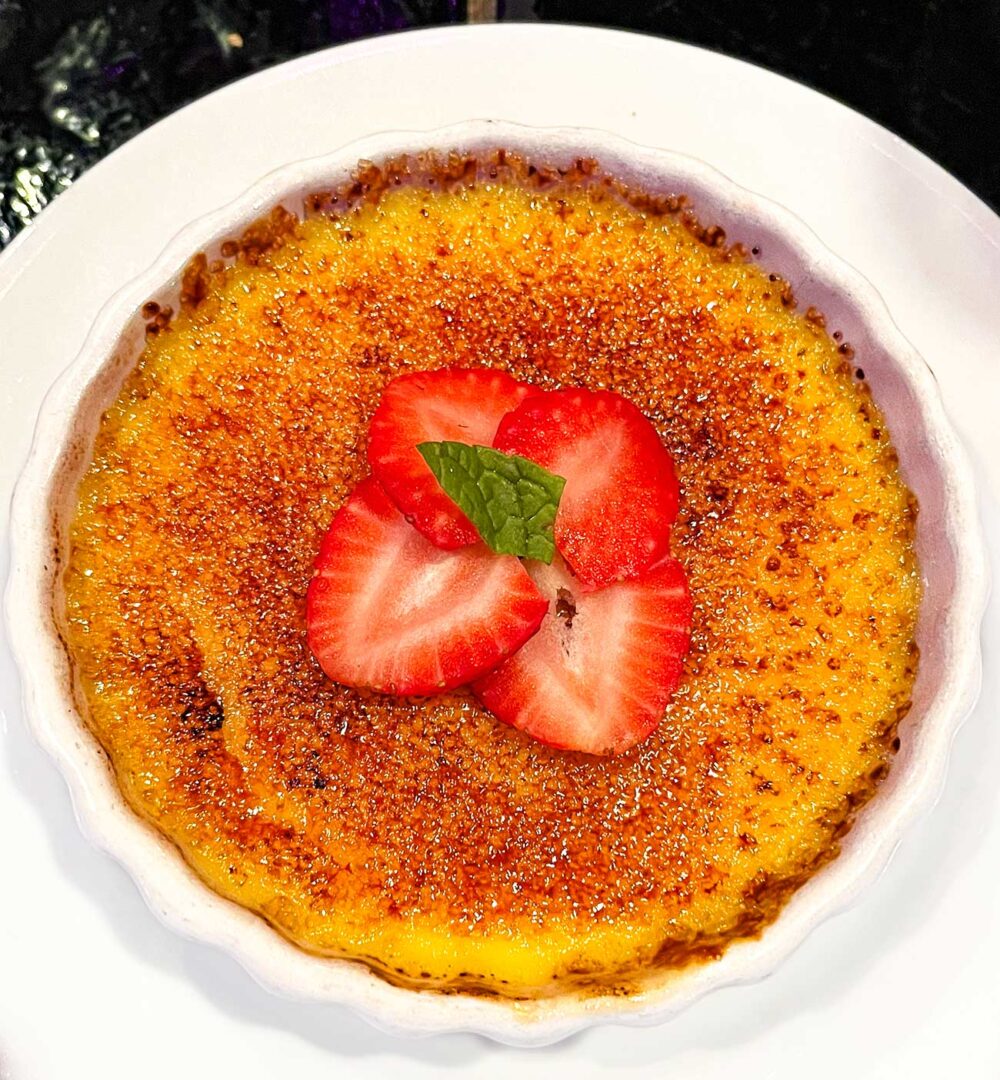 Small ramekin of vanilla bean crème brûlée topped with a sliced strawberry.