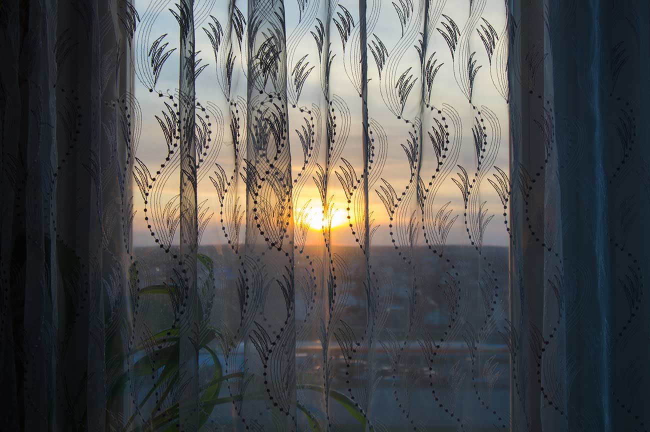View on beautiful sunset from home window through a sheer curtain.