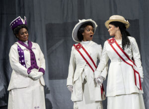 Two women look at each other while another woman stands between them looking away.