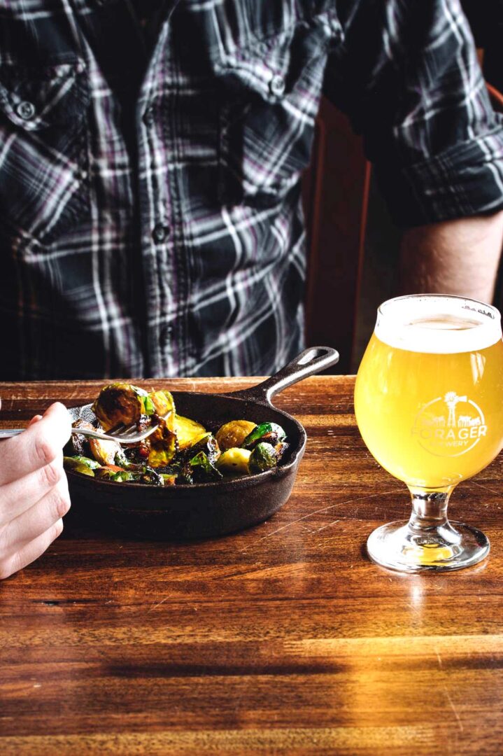 Close-up shot of a mans bowl of food next to a Forager Brewery beer.