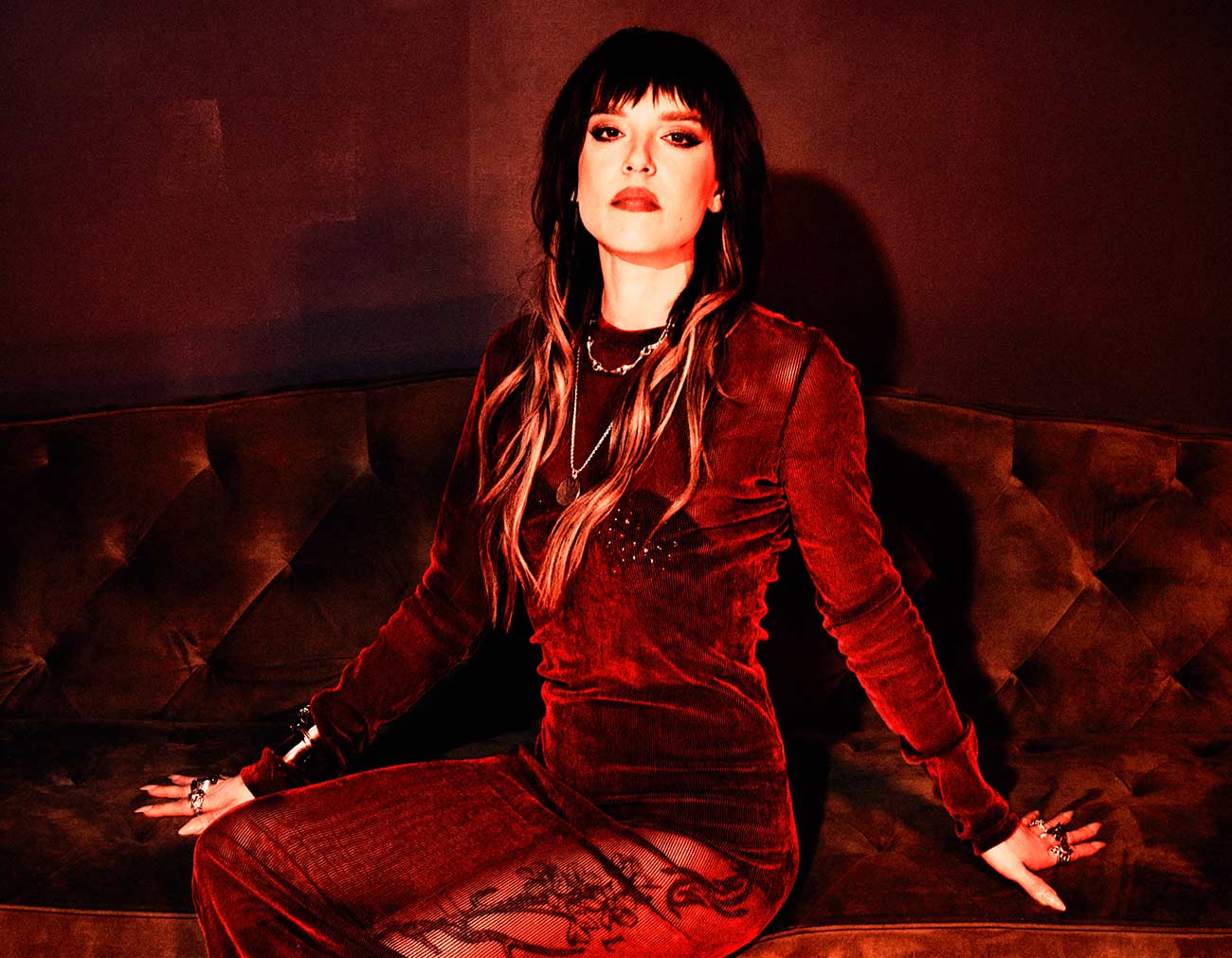 Bisexual hard rock songstress Lzzy Hale poses on a in a velvet dress on a couch.