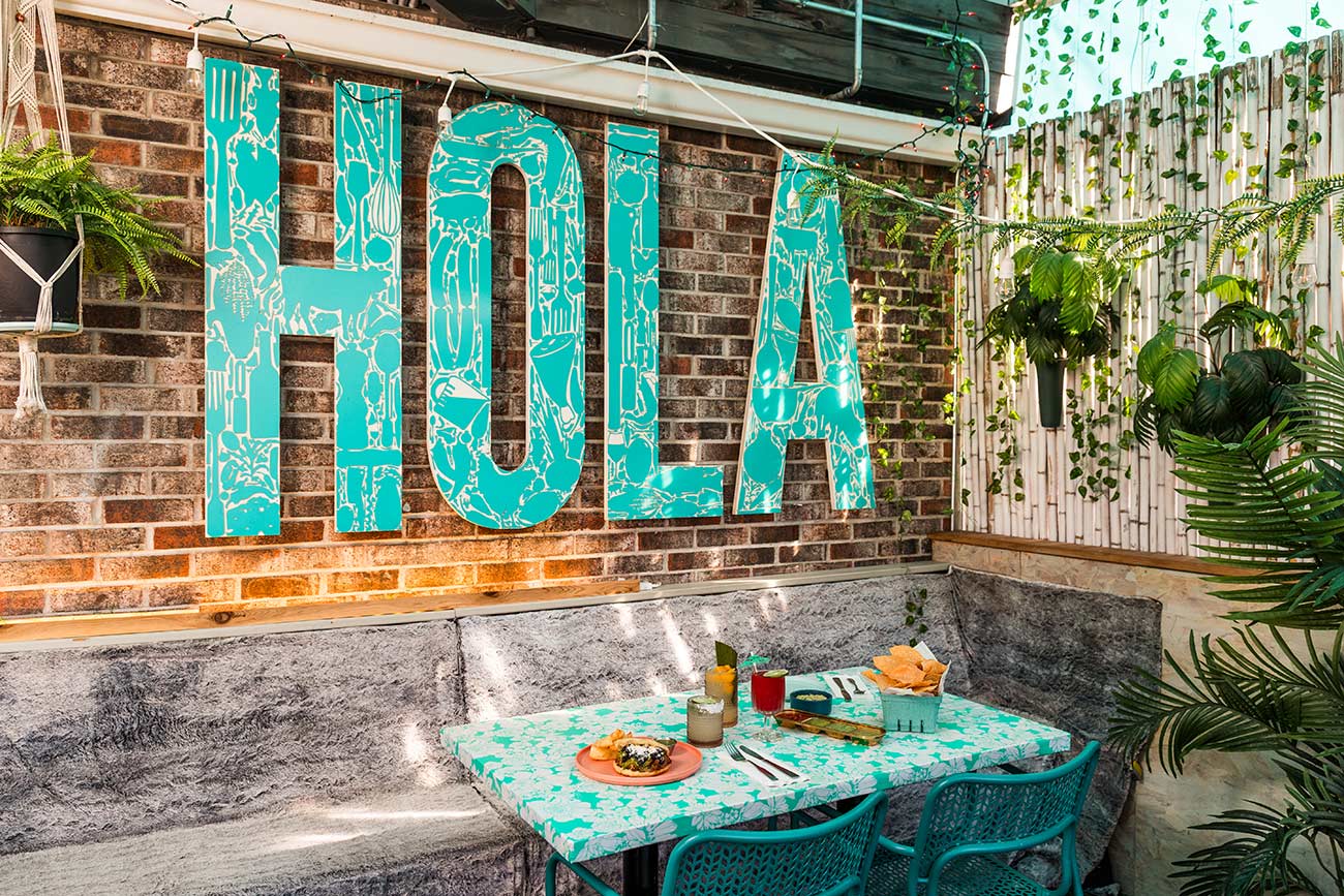 Patio seating at Hola Arepa that features large teal letters that say HOLA.