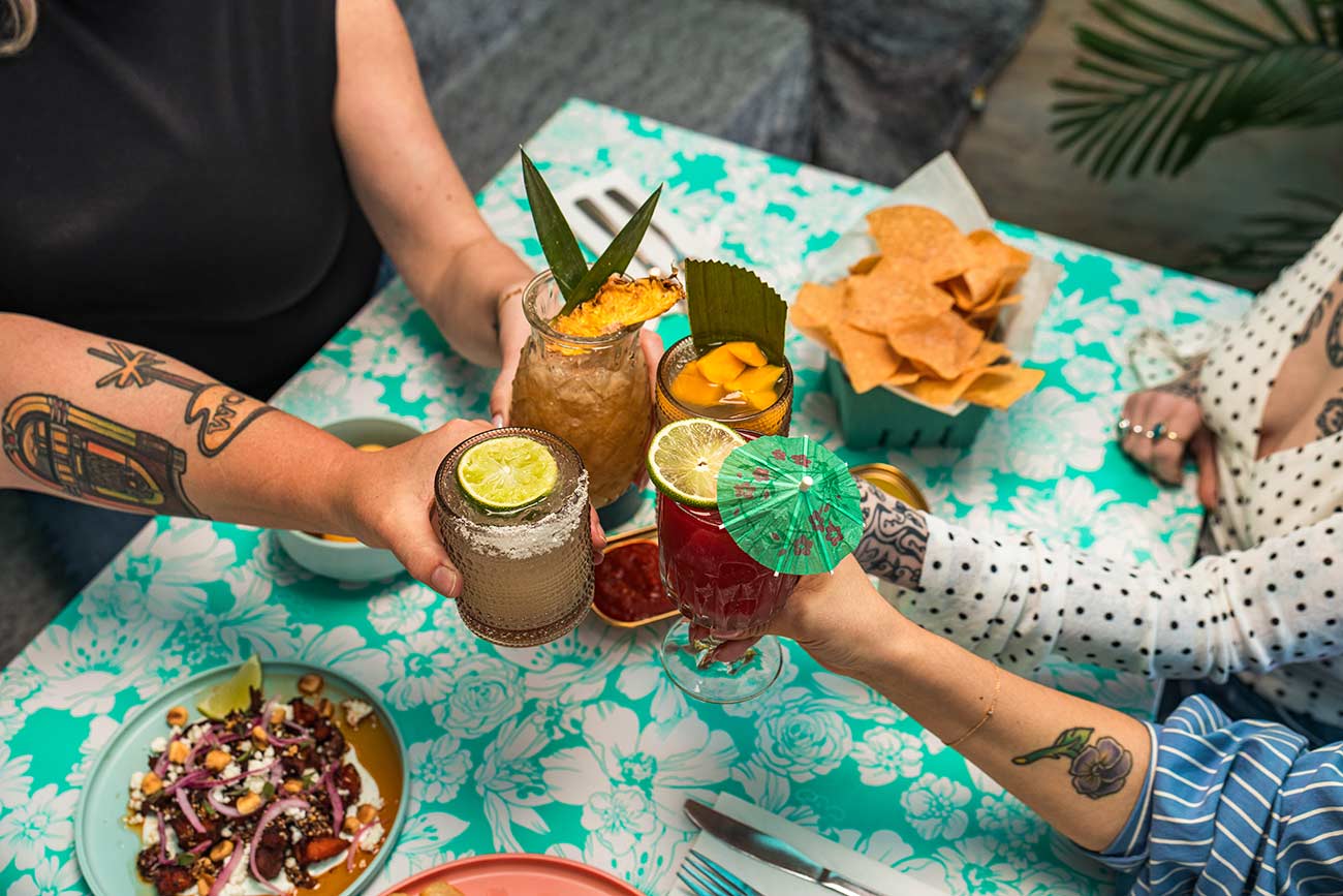 Close-up of four people cheering with craft cocktails in their hands.