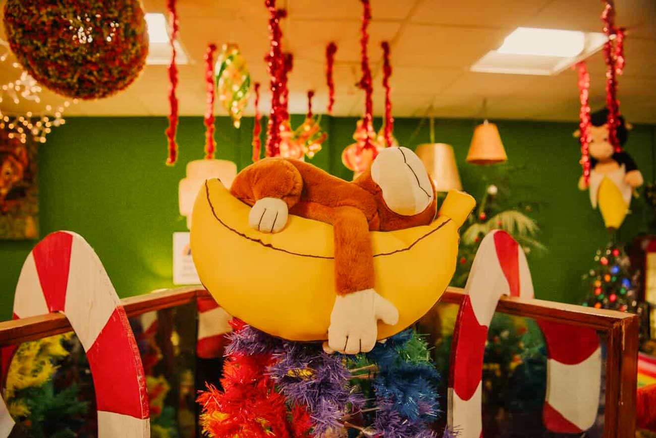 Plush monkey lying on a plush banana hanging from the ceiling at The Clapping Monkey Cafe.
