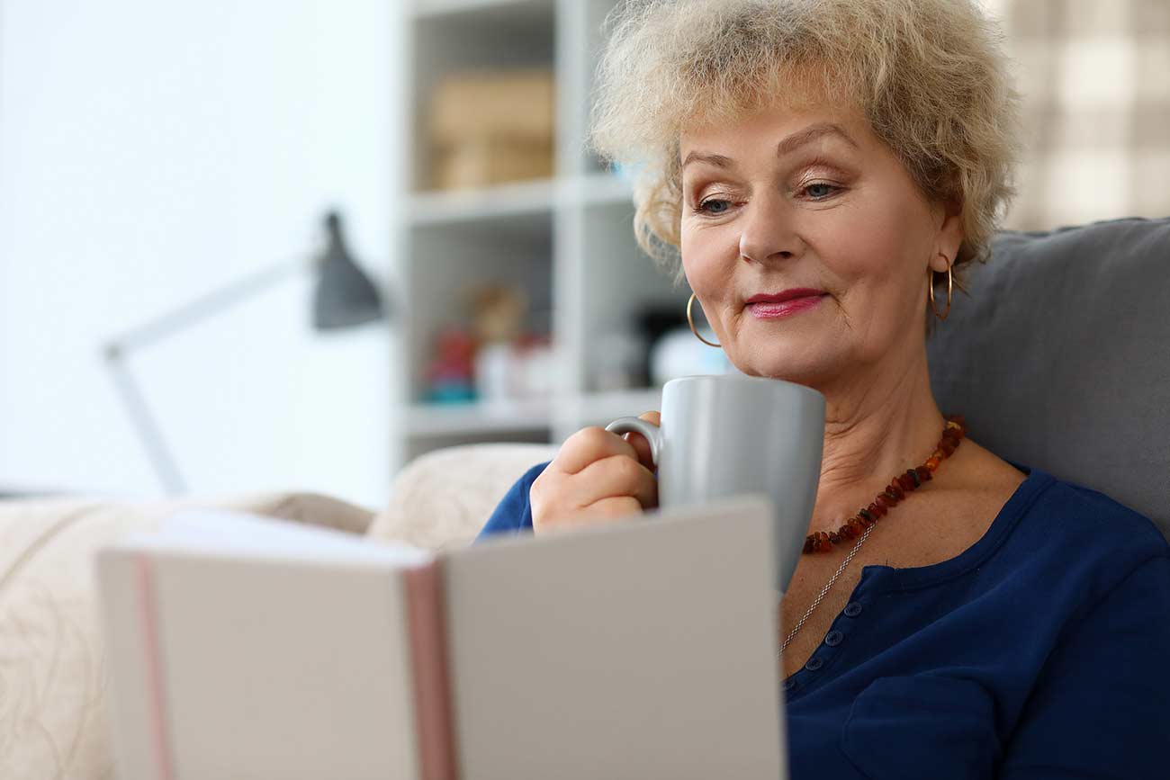 Older woman reading book and drinking herbal tea.