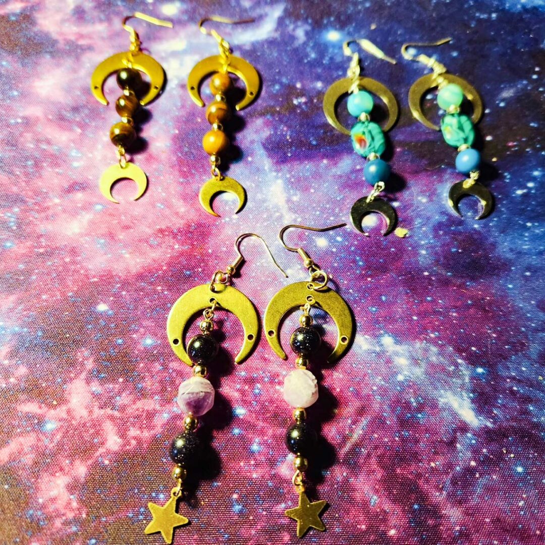 Moon and stars dangle earrings laying on a cosmic background.