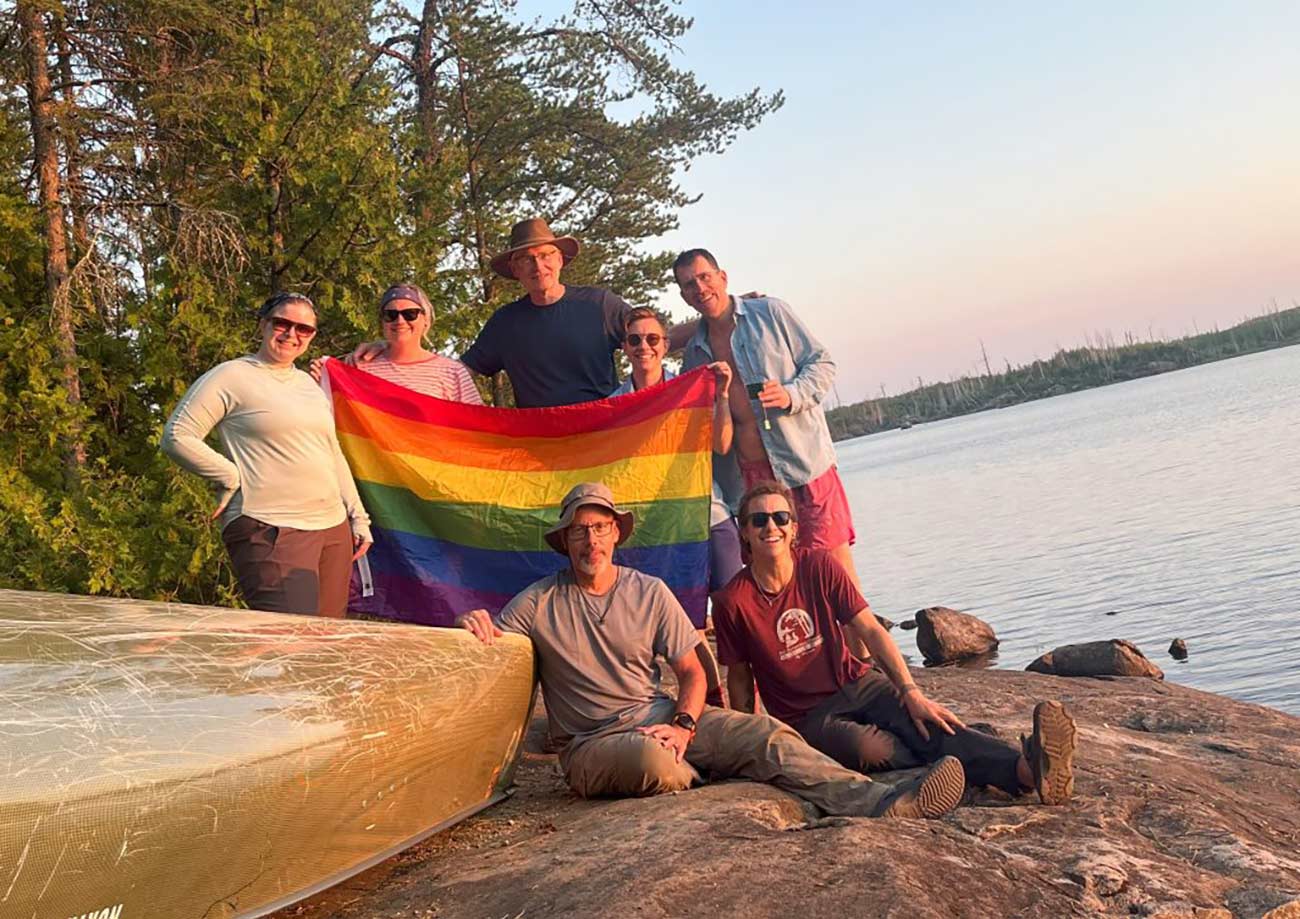 Ely Outfitting Company's LGBTQ+ crew on the trail pose with a rainbow flag.
