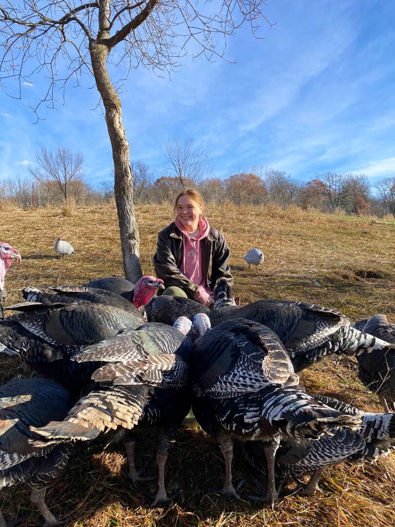 Young woman kneeling next to a flock of turkeys.