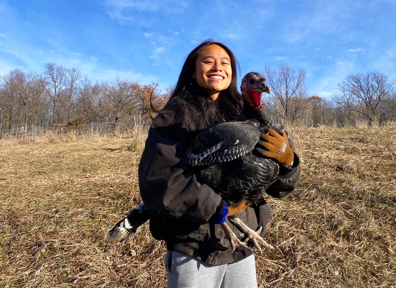 Young woman smiling while holding a live turkey in her arms.