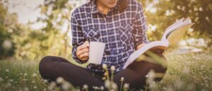 Young woman with coffee sitting on the grass and reading a book.