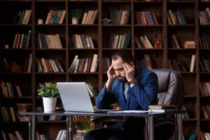 A stressed man suffers from a headache sitting in the office with a laptop.