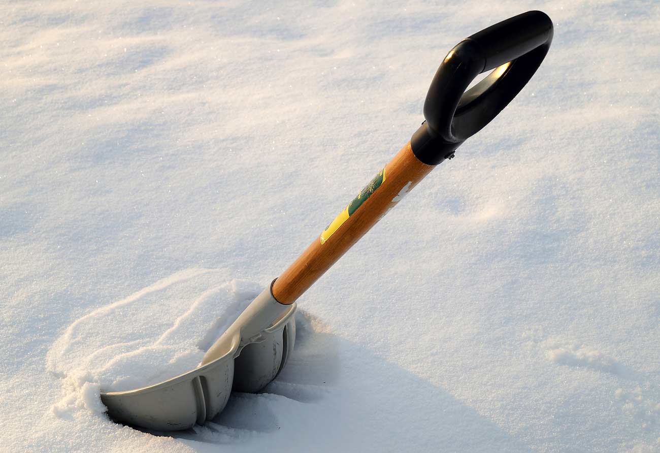Gray plastic snow shovel in fresh snow after a winter storm.
