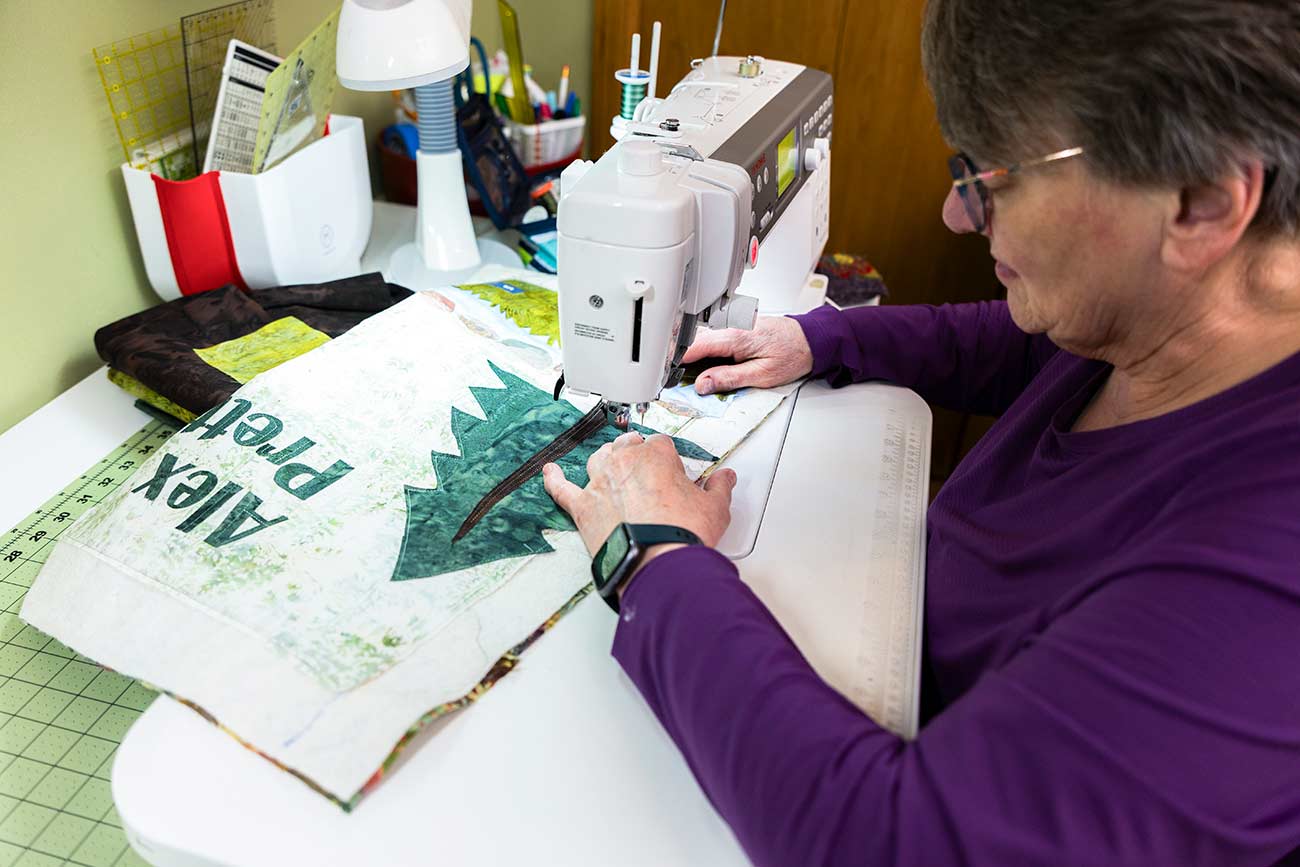 A woman sewing a decal onto a quilt.