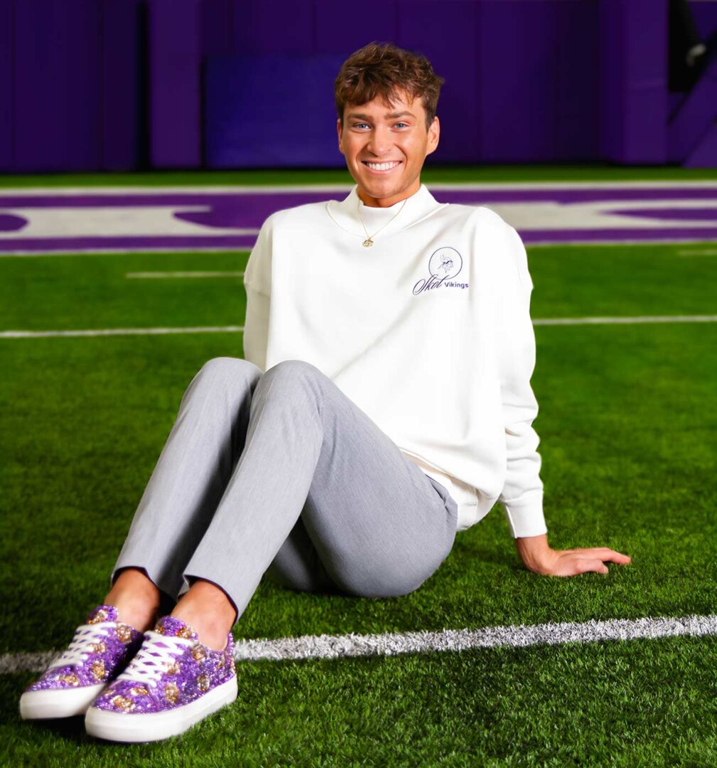 Minnesota Vikings Cheerleader Louie Conn sitting on the Vikvings training field smiling.