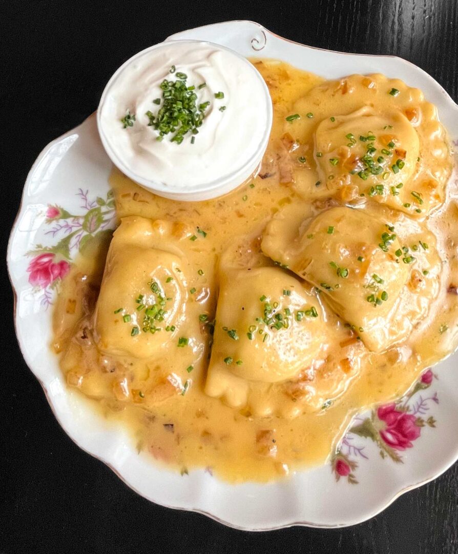 Pierogis stuffed with farmer’s cheese, potato, and onion, served with sour cream on a shell shaped plate.